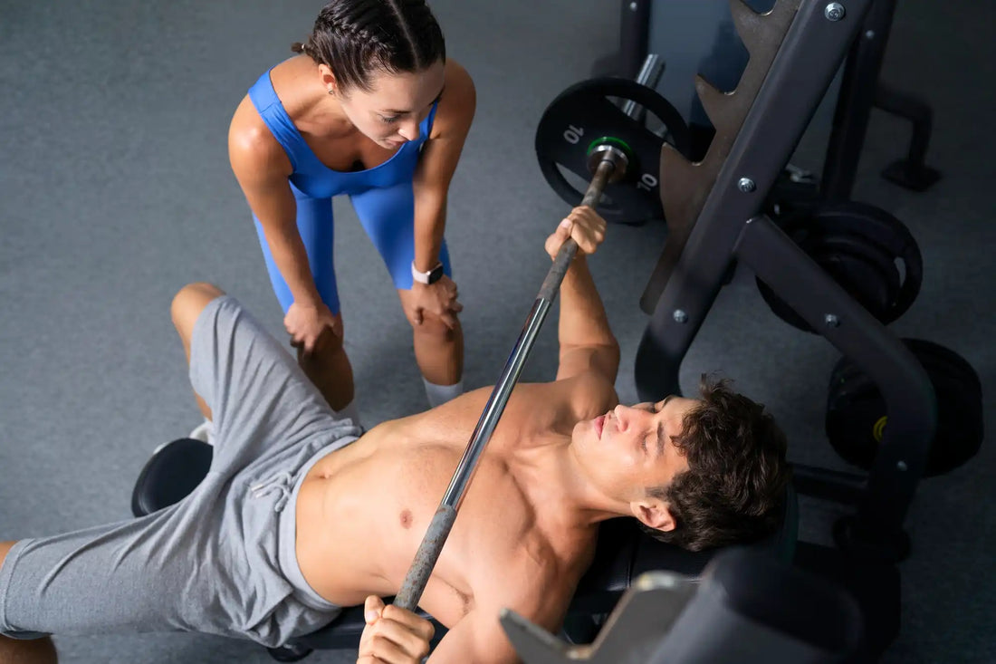 Hombre levantando pesas en un gimnasio en compañía de una mujer que está alentandolo 