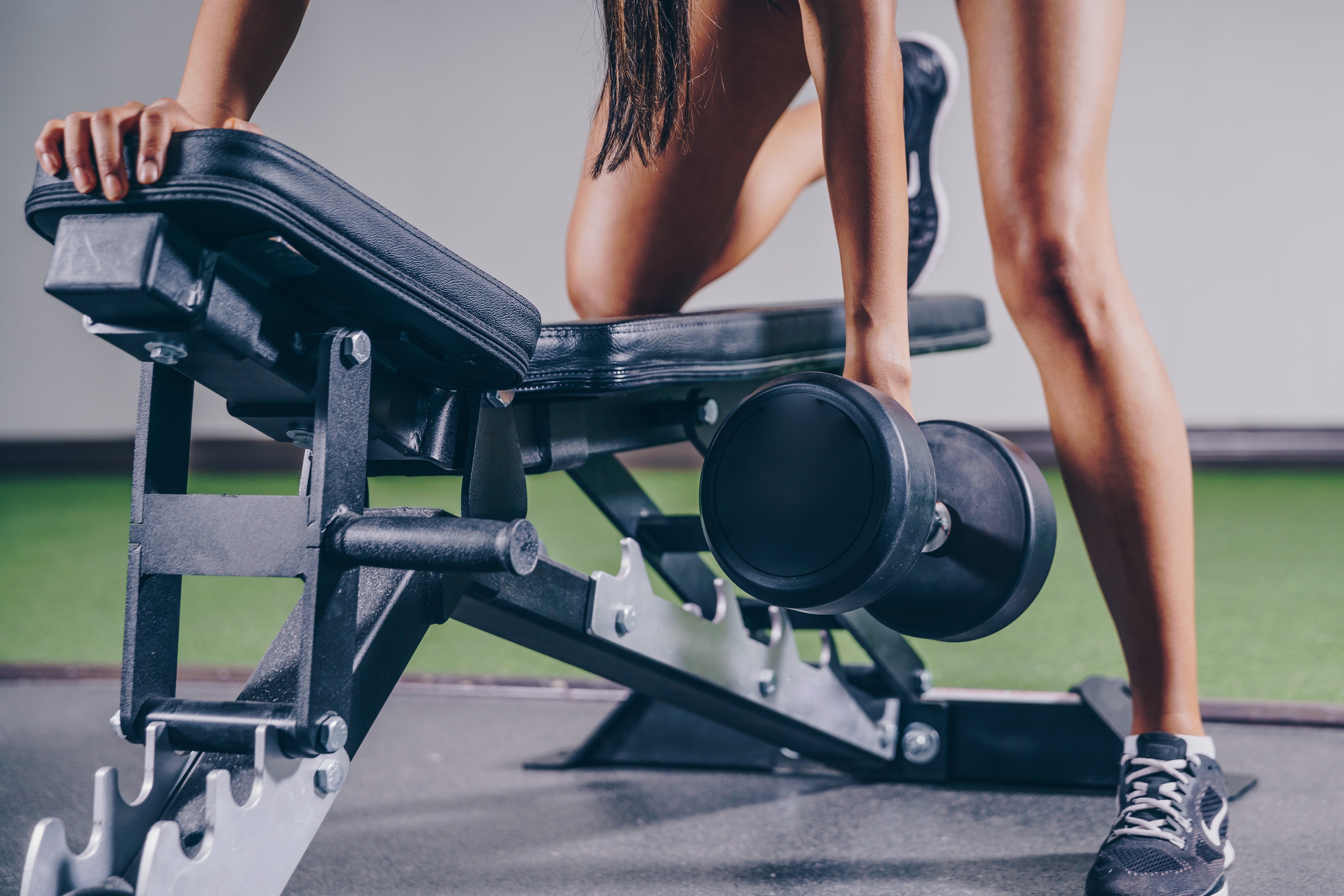 Mujer apoyada sobre un banco de gym para hacer remo de espalda con una mancuerna
